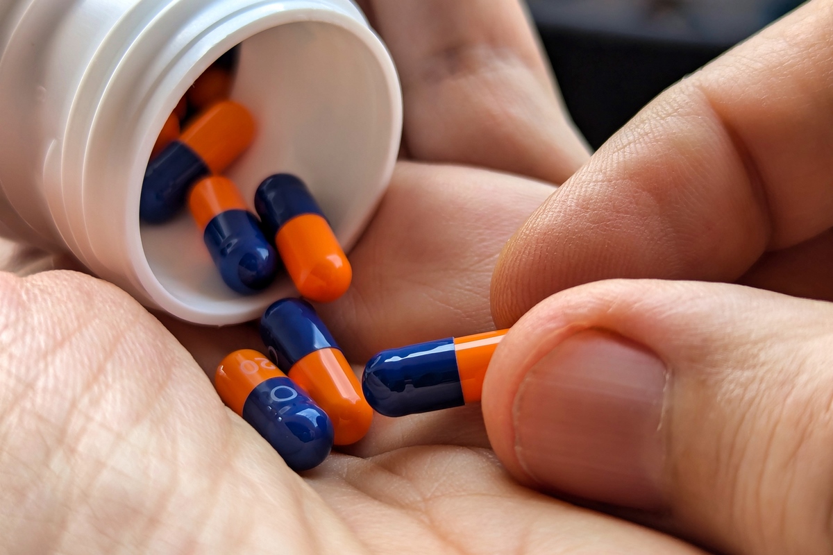 1 de 1 Close-up das mãos de um homem segurando um pote branco de comprimidos caídos. Metrópole...