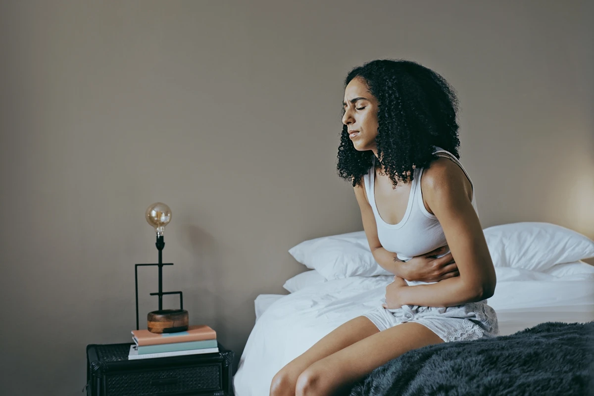 1 de 1 Foto colorida de mulher sentada na cama com dor de barriga - Comeu demais? Saiba como o co...