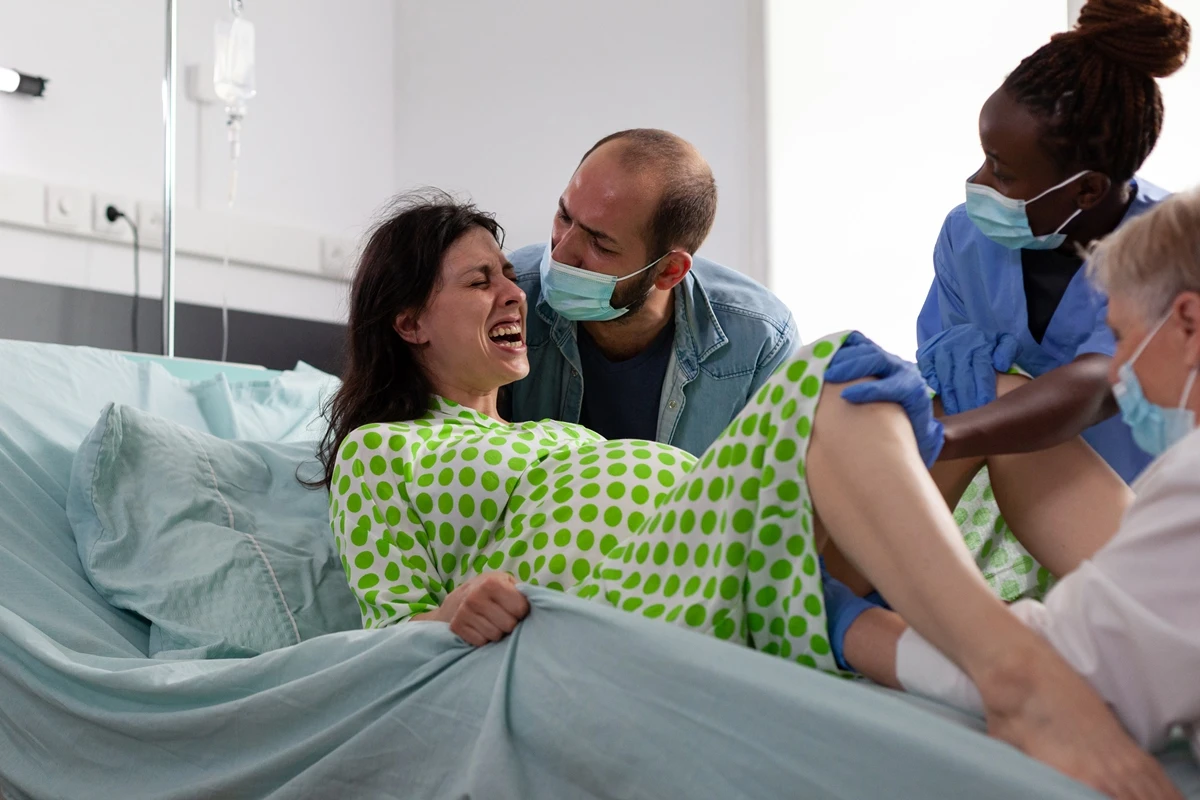 1 de 1 Foto colorida de mulher em trabalho de parto, deitada numa cama, acompanhada de médicos -...
