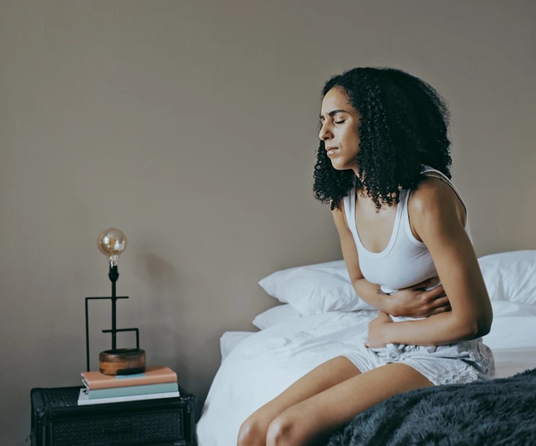 1 de 1 Foto colorida de mulher sentada na cama com dor de barriga - Comeu demais? Saiba como o co...