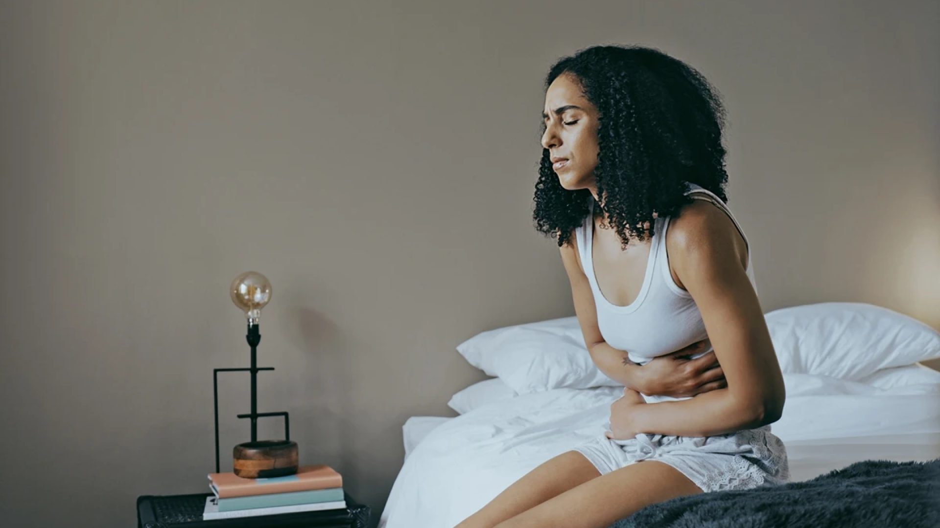 1 de 1 Foto colorida de mulher sentada na cama com dor de barriga - Comeu demais? Saiba como o co...