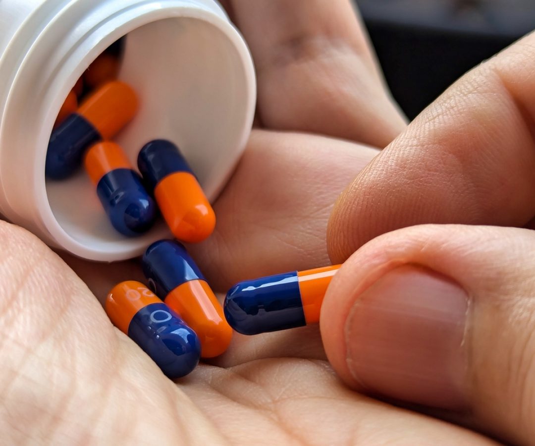 1 de 1 Close-up das mãos de um homem segurando um pote branco de comprimidos caídos. Metrópole...