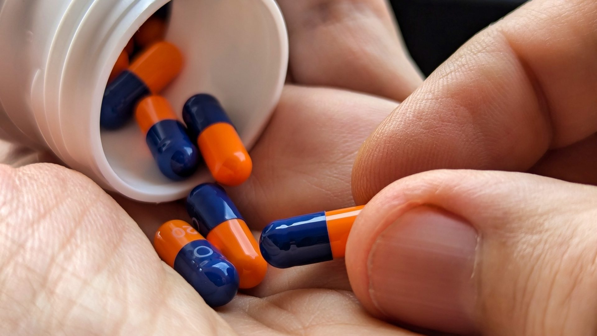 1 de 1 Close-up das mãos de um homem segurando um pote branco de comprimidos caídos. Metrópole...