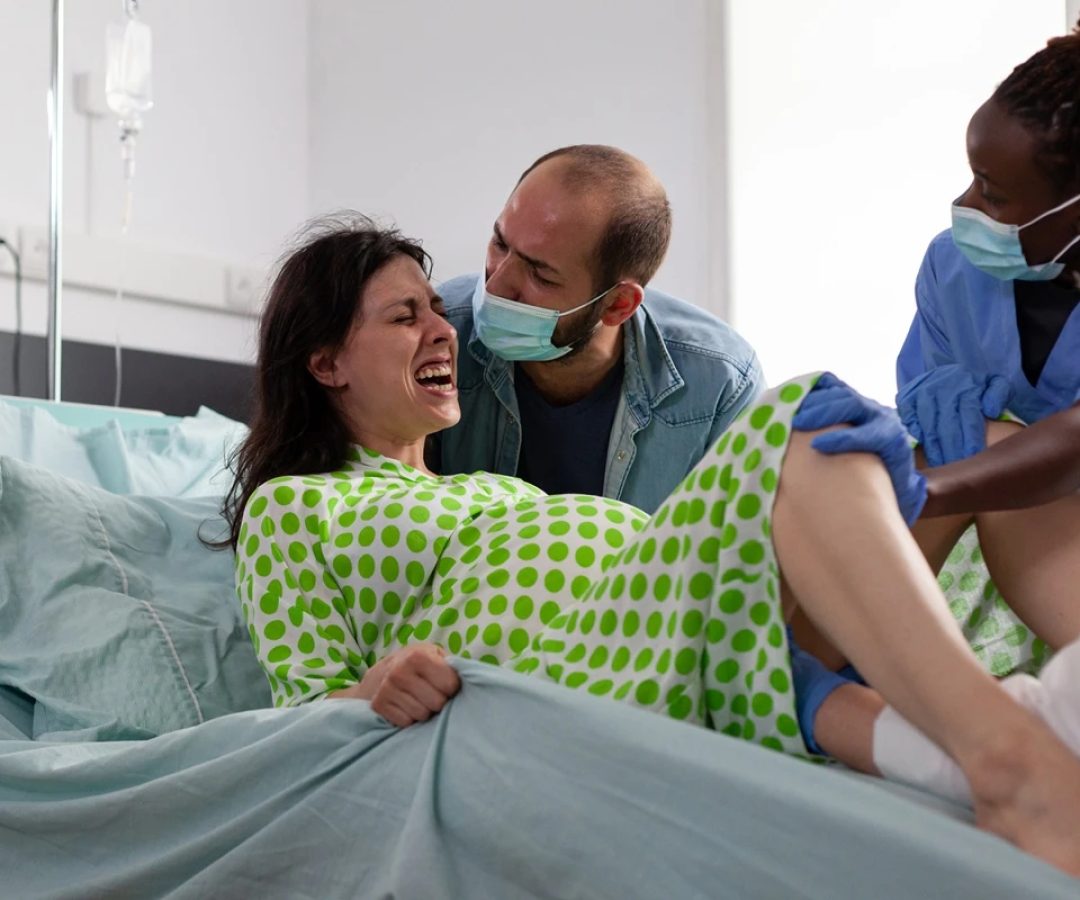 1 de 1 Foto colorida de mulher em trabalho de parto, deitada numa cama, acompanhada de médicos -...