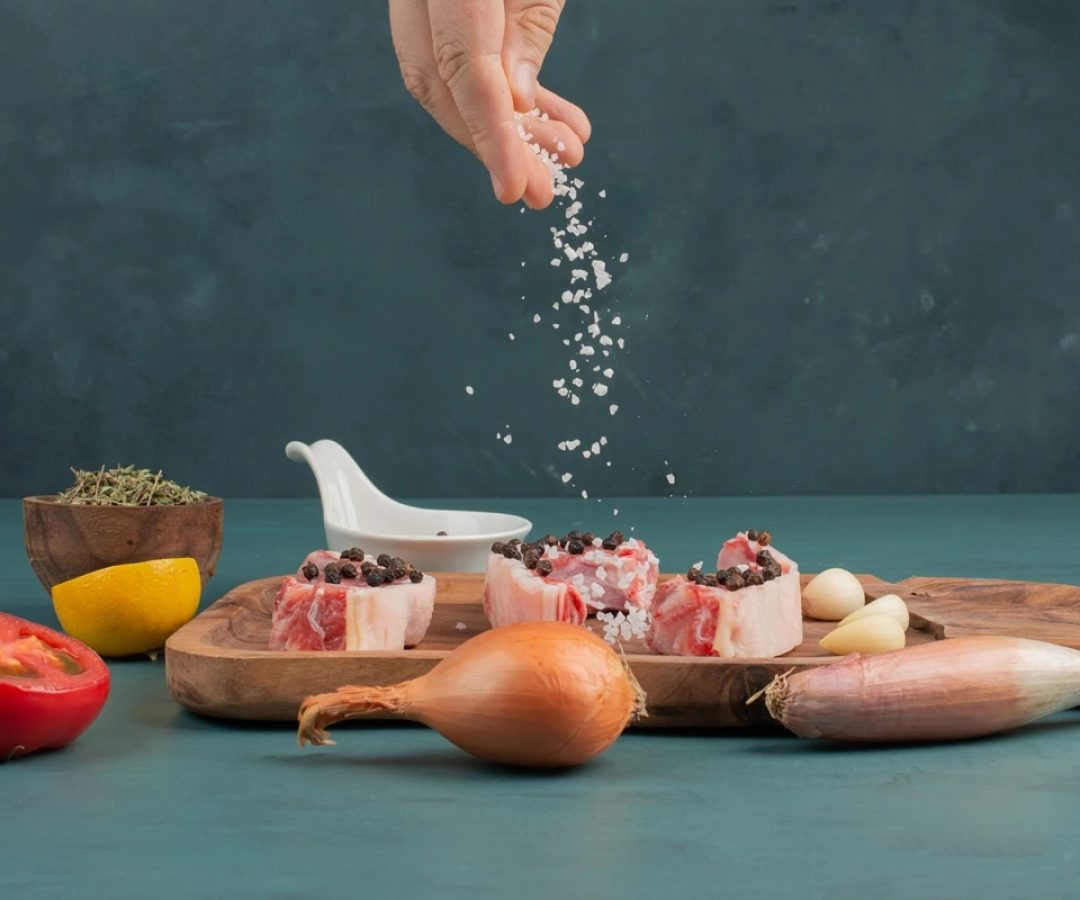 1 de 1 Foto colorida de uma mão colocando sal que tempera uma tipo de carne numa tábua de madei...
